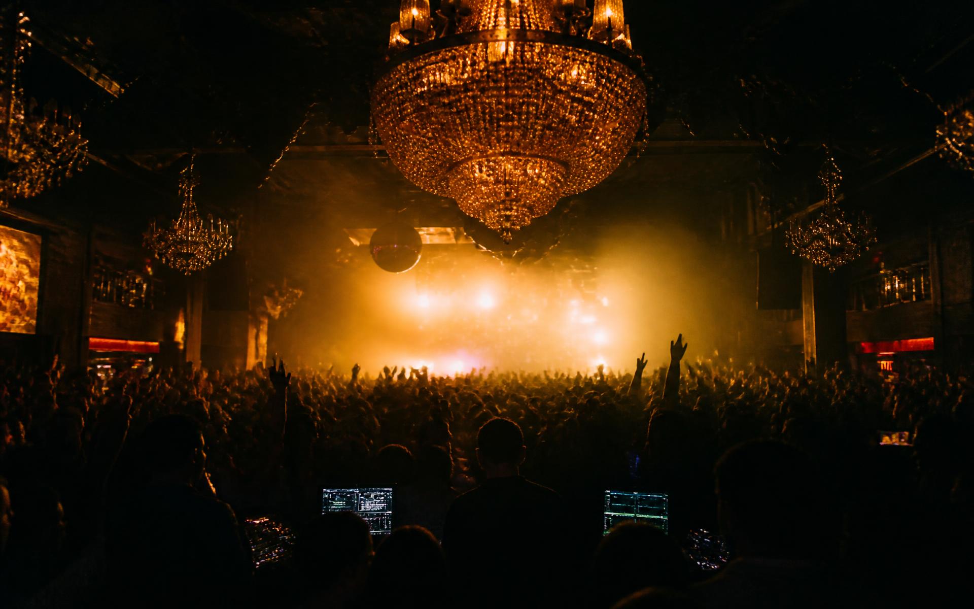 Crowded nightclub with chandeliers and warm stage lighting